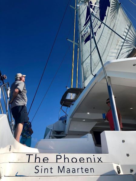 Guest standing on deck of Sail The Phoenix looking up at its billowing white mainsail