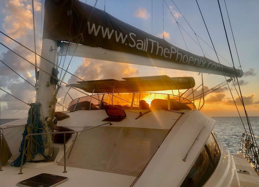 Sail The Phoenix catamaran silhouetted against a fiery orange-pink Caribbean sunset