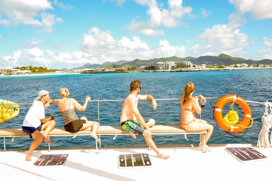 Six guests lounging on the sun bench of Sail The Phoenix with Philipsburg skyline behind
