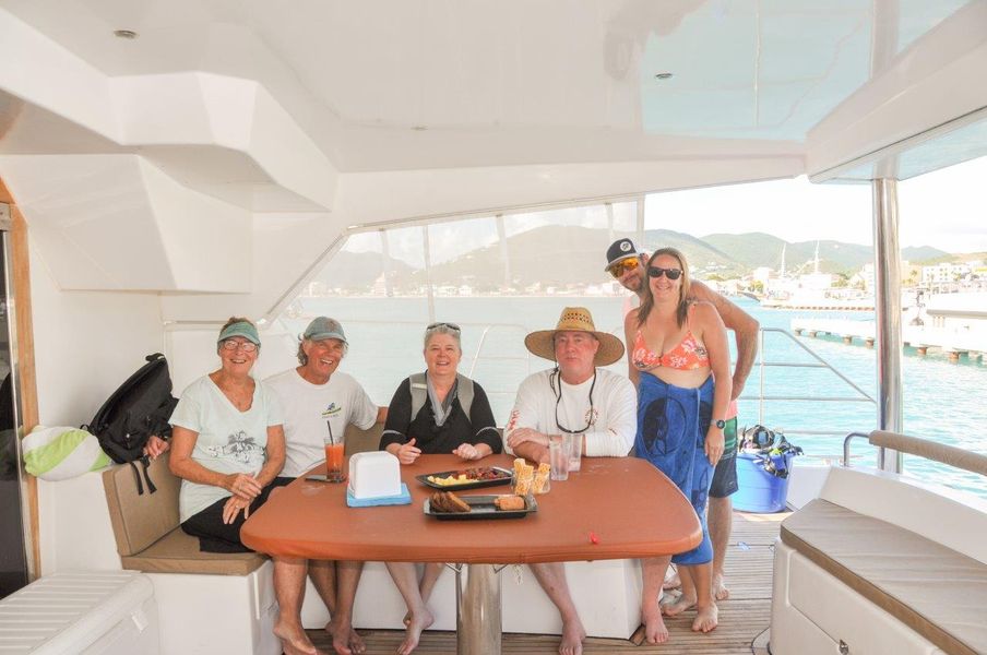 Six guests seated around the aft deck table of Sail The Phoenix smiling and enjoying the day