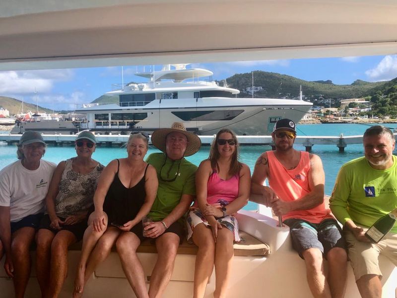 Guests and Captain seated on the aft deck of Sail The Phoenix with a luxury yacht in the background