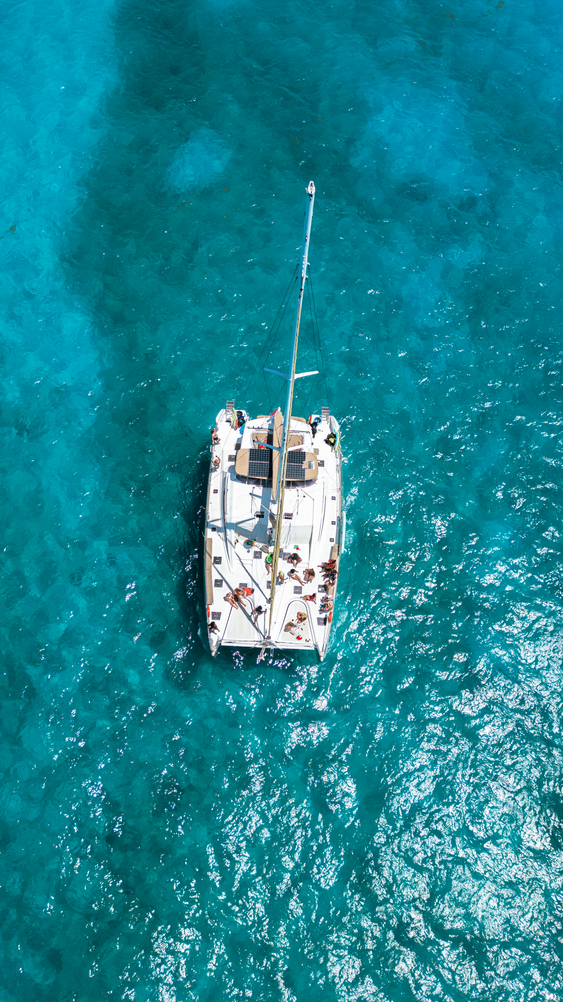 Aerial top-down view of The Phoenix catamaran anchored over turquoise reef, guests on deck
