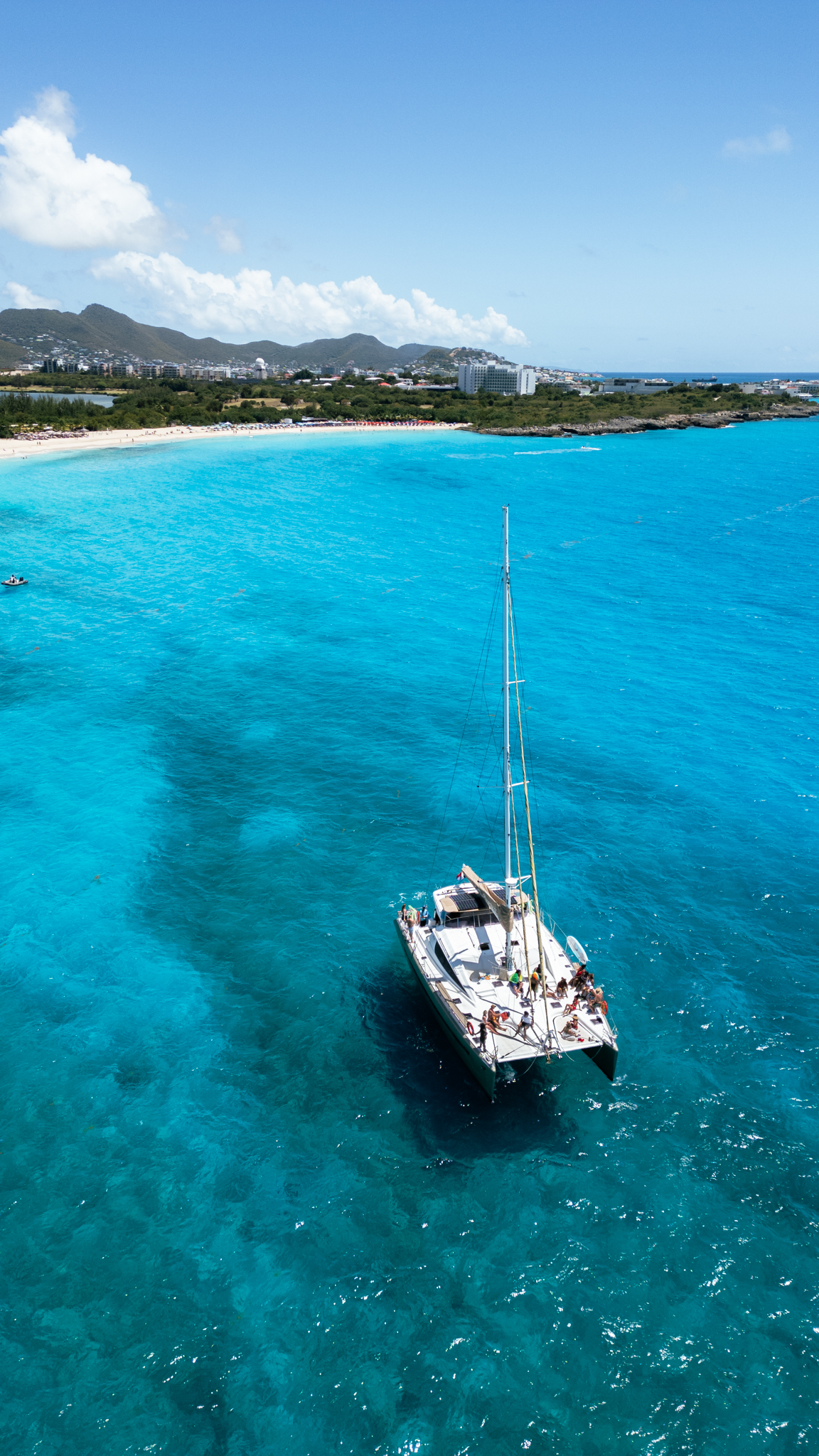 Aerial view of The Phoenix catamaran in turquoise water with St. Maarten coastline and beach behind