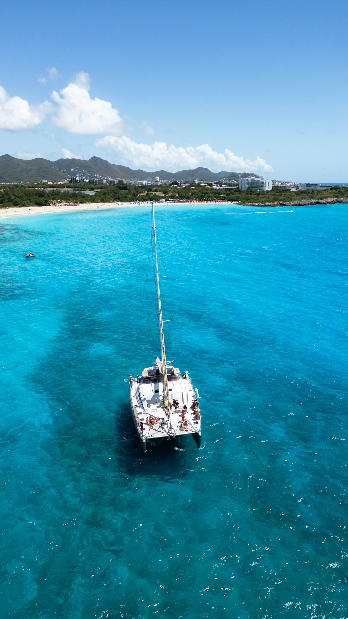Aerial view of The Phoenix catamaran sailing in brilliant turquoise Caribbean water near St. Maarten beach