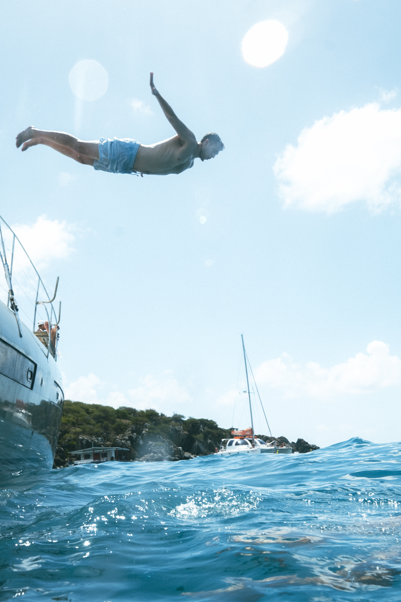 Guest diving off The Phoenix catamaran into crystal clear Caribbean water at Little Bay
