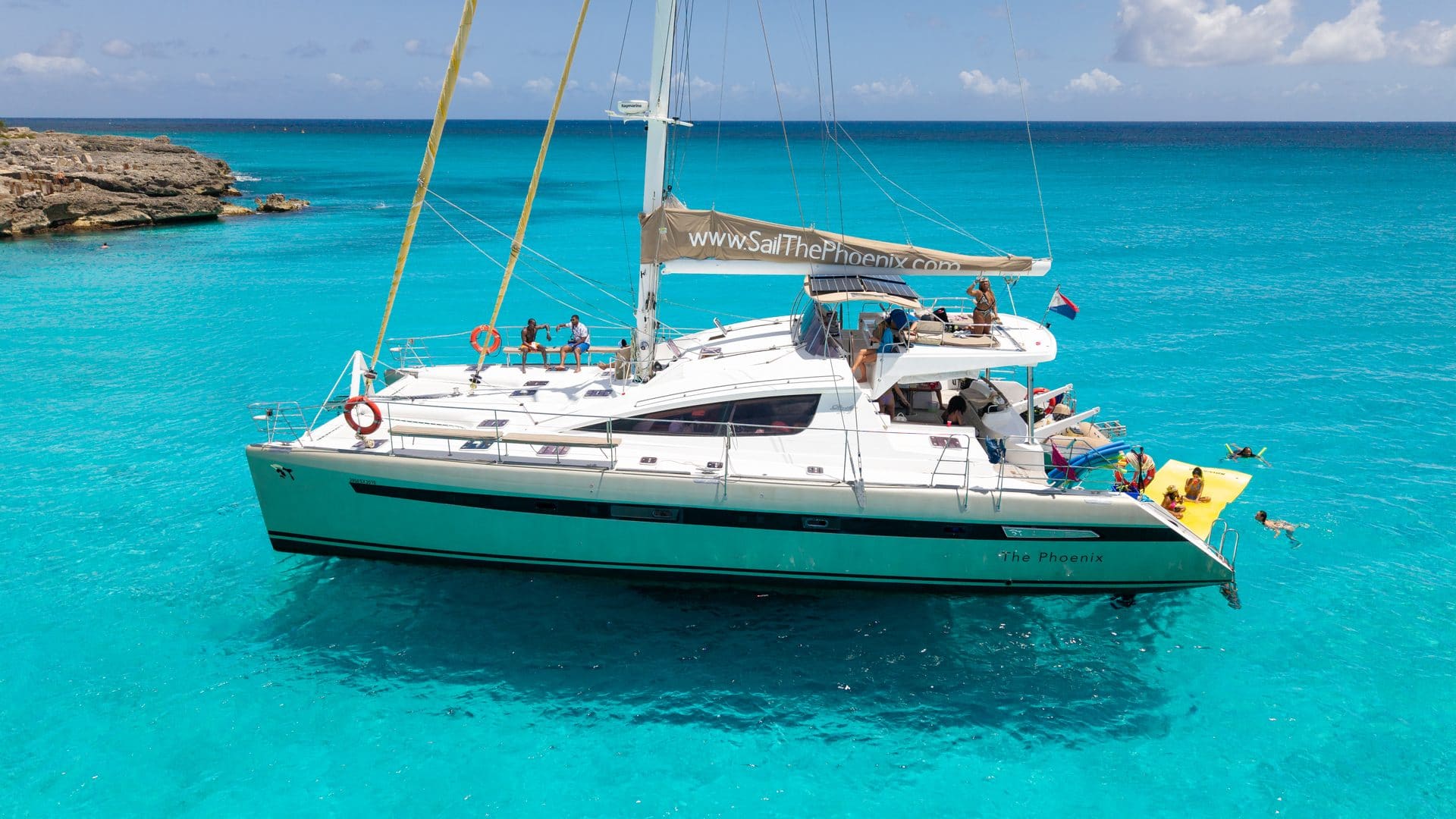 Wide side view of The Phoenix catamaran in bright turquoise water with lily pad deployed